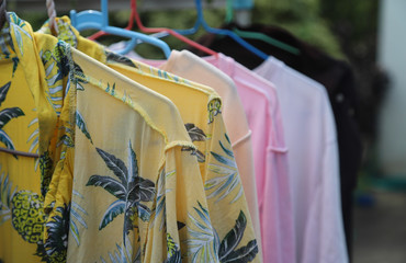 Closeup of yellow shirt and others hanging on hangers for drying under sunlight with natural background. The way of energy saving for global warming reduction. 