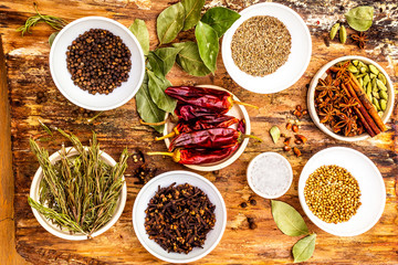 Set of different spices and herbs - black pepper, allspice, rosemary, cumin, hot pepper, bay leaf, coriander, cardamom, star anise, cinnamon sticks, salt. On wooden bark background, top view.