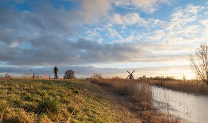 Woman cycling in the Dutch countryside near a traditional windmill. Groningen, the Netherlands.