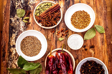 Set of different spices and herbs - allspice, cumin, hot pepper, bay leaf, coriander, cardamom, star anise, cinnamon sticks, salt. On wooden bark background, top view.