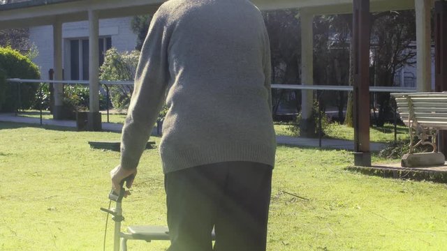 Elderly man using walker at rehab clinic garden with sun light coming from the sky, health care concept