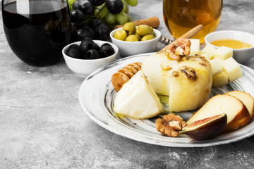 Snacks with wine - various types of cheeses, figs, nuts, honey, grapes on a gray background. Copy space. Food background