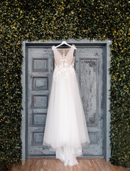 White wedding dress of bride hangs on background of door, boho and rustic style