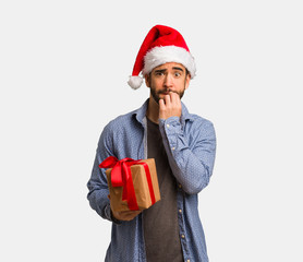 Young man wearing santa hat biting nails, nervous and very anxious