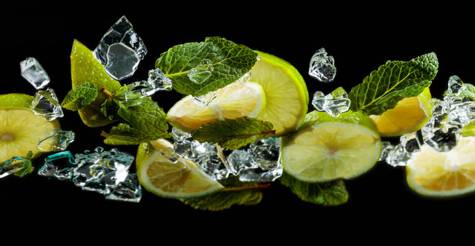 Lime pieces with leaves of peppermint on black background.