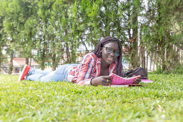 Afroamerican girl laying down on the grass making school lesson