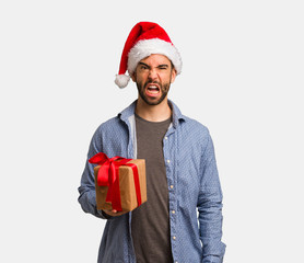 Young man wearing santa hat screaming very angry and aggressive