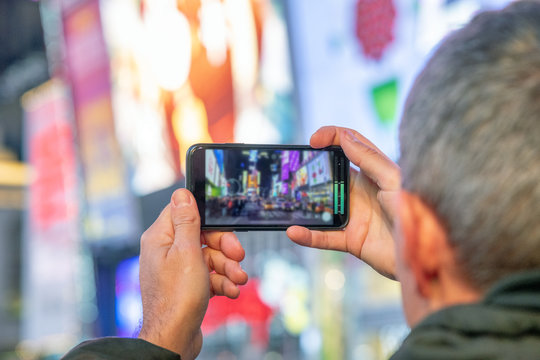 Man taking pictures of Times Square at night with smartphone
