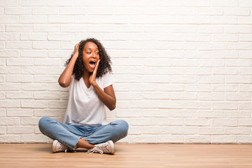 Young black woman sitting on a wooden floor laughing and having fun, being relaxed and cheerful, feels confident and successful