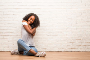 Young black woman sitting on a wooden floor proud and confident, pointing fingers, example to follow, concept of satisfaction, arrogance and health