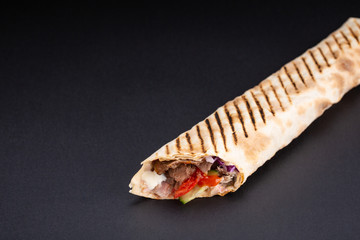Shawarma sandwich - fresh roll of thin lavash or pita bread filled with grilled meat, mushrooms, cheese, cabbage, carrots, sauce, green. Traditional Eastern snack. On black background.