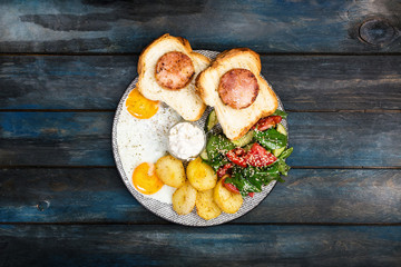 Big delicious breakfast with fried eggs, fried potatoes, fresh salad, chicken ham on bread and cream sauce. Top view.