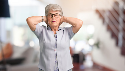 Beautiful senior woman covering ears with hands, angry and tired of hearing some sound at home.