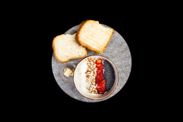 Healthy breakfast. Rice cereal or porridge with fresh strawberry, almond and coconut flakes, served with bread and butter. Isolated on the black background, top view