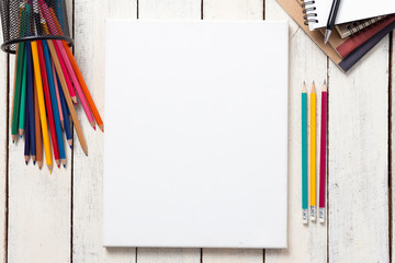 Empty white canvas frame and colorful pencils on whit wooden table