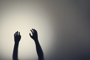 Dark silhouette of woman hands behind glass door. Concept of depression, fear, panic attacks
