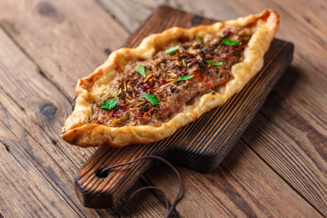 Turkish handmade pide lies on an old brown wooden table. Cherry tomatoes, parsley, lemon, hot pepper, garlic are on the table.