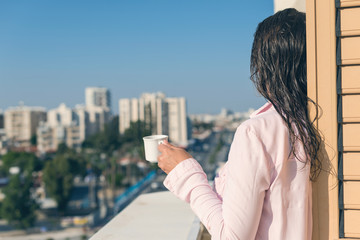 Fototapeta premium Woman with wet hear in a pink shirt with cup of coffee at the summer morning against the background of town