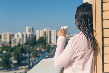Fototapeta na wymiar Woman with wet hear in a pink shirt with cup of coffee at the summer morning against the background of town