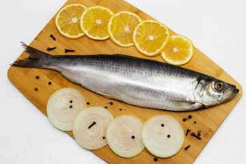 Herring on a cutting board with onions and lemon
