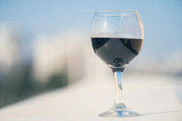 Close up of glass of red wine against the background of blurred town with bokeh at summer evening