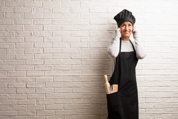 Young baker indian woman against a bricks wall covering ears with hands, angry and tired of hearing some sound