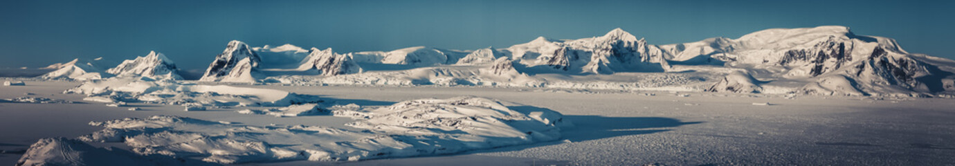 Panorama view of Antarctica nature, sunlit snow covered Penola bay. Stunning aerial shot. The ice surface of the South Pole. Picturesque snow covered mountains next to the frozen Antarctic shoreline