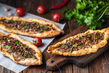Turkish handmade pide lies on an old brown wooden table. Cherry tomatoes, parsley, lemon, hot pepper, garlic are on the table.