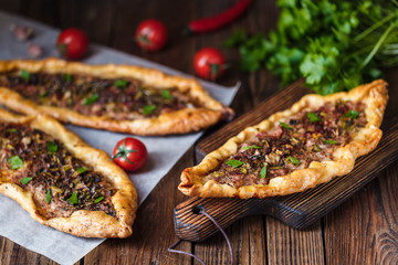 Turkish handmade pide lies on an old brown wooden table. Cherry tomatoes, parsley, lemon, hot pepper, garlic are on the table.