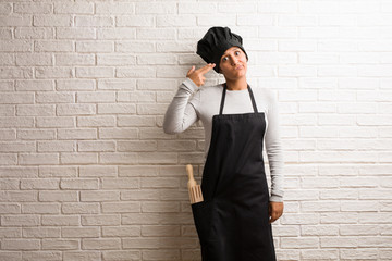 Young baker indian woman against a bricks wall making a suicide gesture, feeling sad and scared forming a gun with fingers