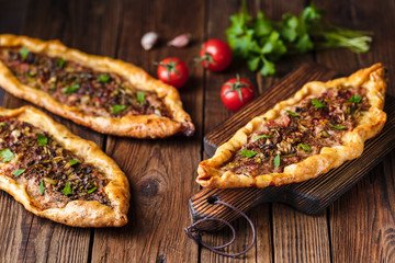 Turkish handmade pide lies on an old brown wooden table. Cherry tomatoes, parsley, lemon, hot...