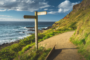 Close-up crossroad signpost. Northern Ireland shoreline. The hiking trail next to the Irish shore. Grass covered hill over the ocean. The wooden road sign on the tourist path. Stunning landscape.