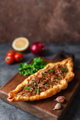 Turkish handmade pide lies on an blue surface. Cherry tomatoes, parsley, lemon, hot pepper, garlic are on the table.