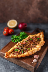 Turkish handmade pide lies on an blue surface. Cherry tomatoes, parsley, lemon, hot pepper, garlic are on the table.