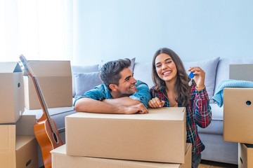 Cheerful and happy young couple holding the keys of their new home with moving cardbox during move...