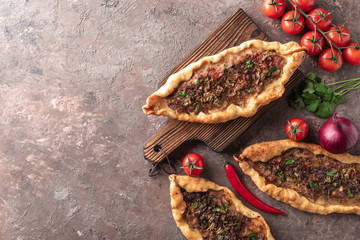 Turkish handmade pide lies on an brown decorative surface. Cherry tomatoes, parsley, lemon, hot...
