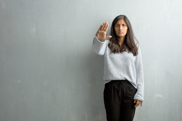 Young indian woman against a grunge wall serious and determined, putting hand in front, stop gesture, deny concept