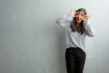 Young indian woman against a grunge wall surprised and shocked, looking with wide eyes, excited by an offer or by a new job, win concept