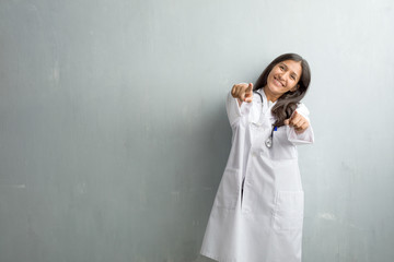 Young indian doctor woman against a wall cheerful and smiling pointing to the front