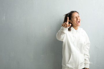 Young sporty indian woman against a gym wall shouting, laughing and making fun of another, concept of mockery and uncontrol