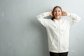 Young sporty indian woman against a gym wall surprised and shocked, looking with wide eyes, excited by an offer or by a new job, win concept