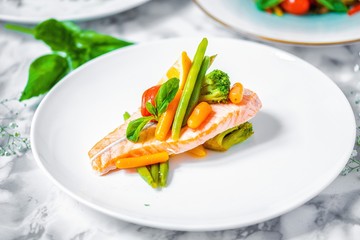 steamed salmon steak with vegetables on a white marble table