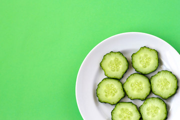 Top view of a plate with sliced cucumber slices on a green background.