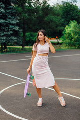 Portrait of a smiling charming brunette female holding her skateboard on a basketball court.