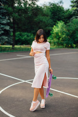 Portrait of a smiling charming brunette female holding her skateboard on a basketball court.