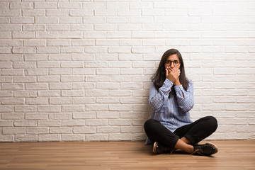 Young indian woman sit against a brick wall covering mouth, symbol of silence and repression, trying not to say anything