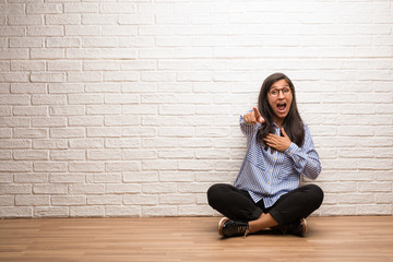 Young indian woman sit against a brick wall shouting, laughing and making fun of another, concept of mockery and uncontrol