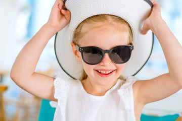 Little laughing blond girl in black sunglasses holding her white hat