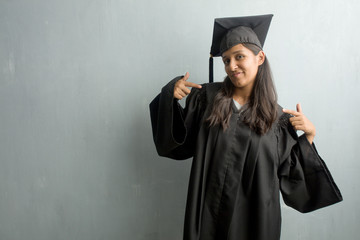 Young graduated indian woman against a wall proud and confident, pointing fingers, example to follow, concept of satisfaction, arrogance and health