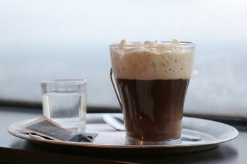 Viennese coffee. Vienna coffee topped with whipped cream with glass of water and metal spoon on a metal tray on a wooden table.